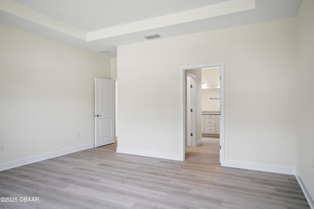 unfurnished bedroom featuring a tray ceiling, light hardwood / wood-style flooring, and ensuite bath