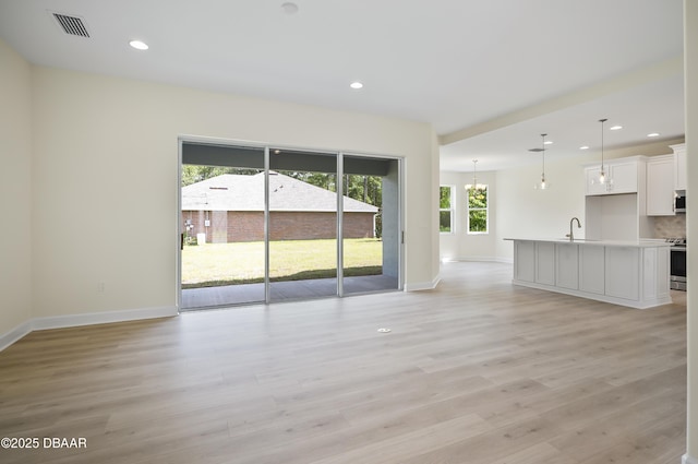 unfurnished living room featuring sink, an inviting chandelier, and light hardwood / wood-style floors