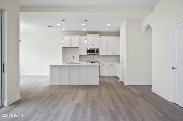 kitchen with white cabinets, an island with sink, tasteful backsplash, sink, and hanging light fixtures