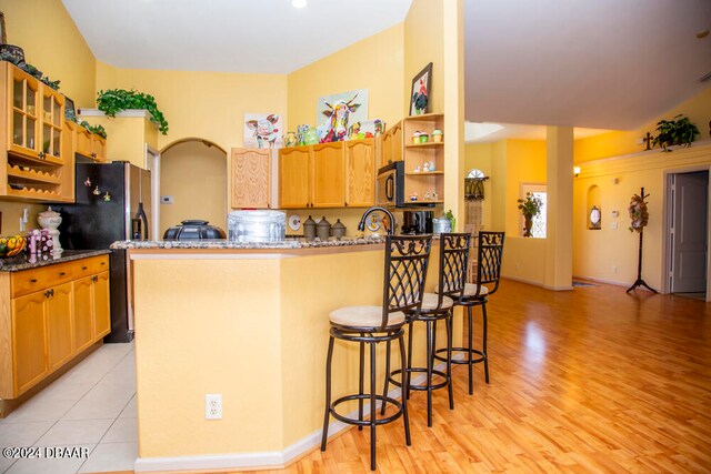 kitchen with kitchen peninsula, light hardwood / wood-style flooring, a breakfast bar area, and dark stone countertops