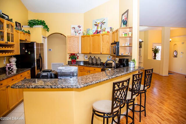 kitchen featuring stainless steel appliances, a kitchen bar, dark stone countertops, kitchen peninsula, and light hardwood / wood-style flooring