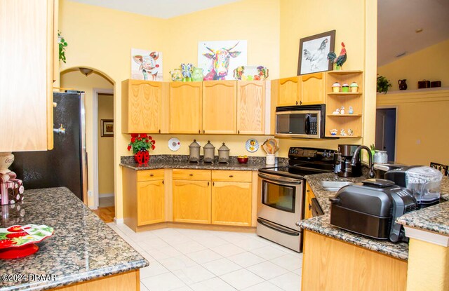 kitchen with kitchen peninsula, appliances with stainless steel finishes, dark stone counters, light tile patterned floors, and vaulted ceiling