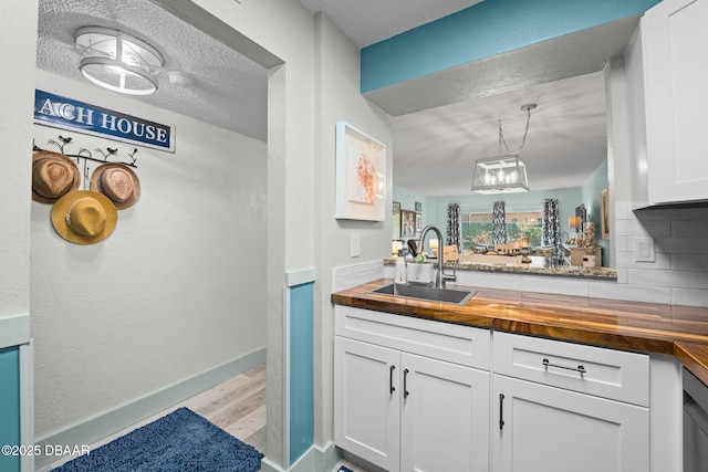 kitchen with wood counters, sink, white cabinets, hanging light fixtures, and a textured ceiling