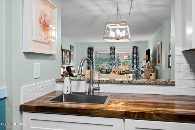 kitchen featuring wood counters, sink, hanging light fixtures, and white cabinets