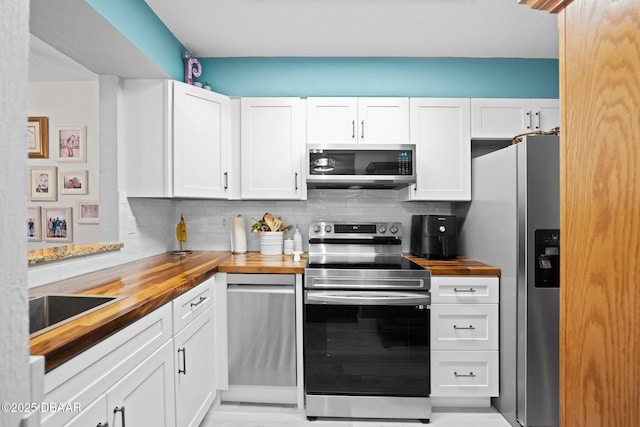 kitchen with appliances with stainless steel finishes, butcher block countertops, sink, white cabinets, and decorative backsplash