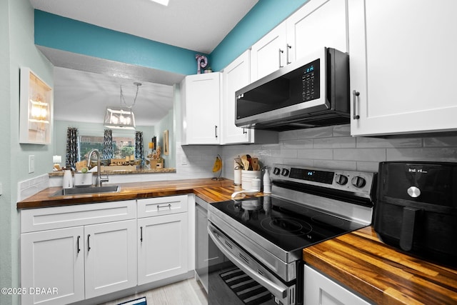 kitchen with appliances with stainless steel finishes, butcher block counters, sink, and white cabinets