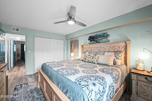 bedroom with ceiling fan, hardwood / wood-style floors, a textured ceiling, and a closet