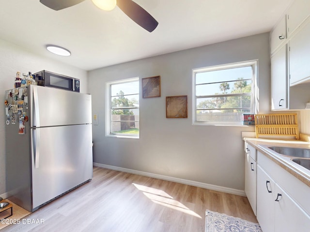 903 Conrad Dr, New Smyrna Beach, FL 32168 - kitchen featuring freestanding refrigerator, black microwave, light wood finished floors, a ceiling fan, and white cabinets