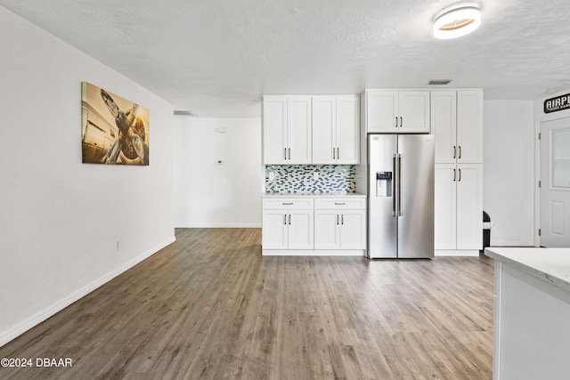 kitchen with tasteful backsplash, stainless steel fridge, white cabinets, and light wood-type flooring