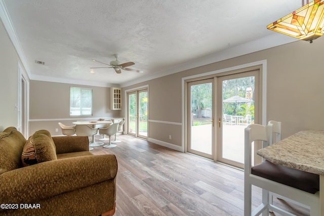 living room featuring ceiling fan, wood-type flooring, ornamental molding, and a textured ceiling