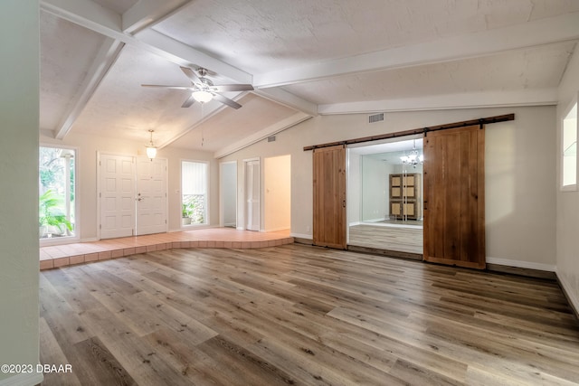 unfurnished living room with ceiling fan, a textured ceiling, wood-type flooring, a barn door, and lofted ceiling with beams