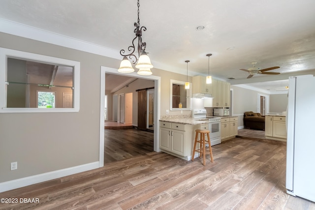 kitchen featuring light stone countertops, hardwood / wood-style floors, a breakfast bar area, white appliances, and cream cabinetry