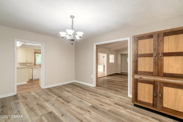 unfurnished room featuring light hardwood / wood-style flooring, a textured ceiling, and an inviting chandelier