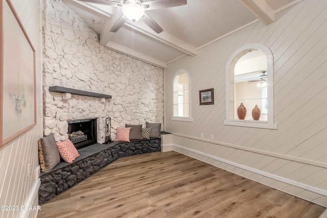 living room featuring a stone fireplace, wooden walls, hardwood / wood-style flooring, and ceiling fan