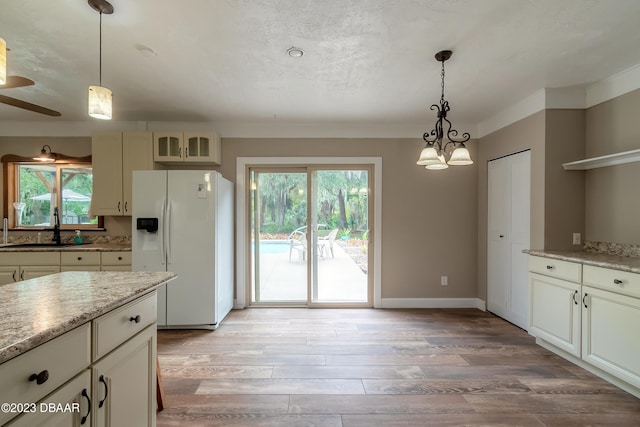 kitchen featuring light wood-type flooring, white fridge with ice dispenser, hanging light fixtures, and sink