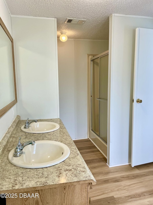 1910 Woodcrest Dr, Ormond Beach, FL 32174 - bathroom with a shower stall, wood finished floors, a textured ceiling, and double vanity