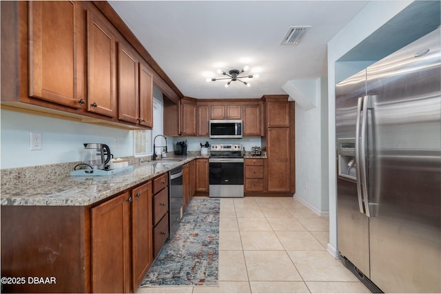 127 Bosarvey Dr, Ormond Beach, FL 32176 - kitchen with appliances with stainless steel finishes, brown cabinetry, light tile patterned floors, and light stone counters