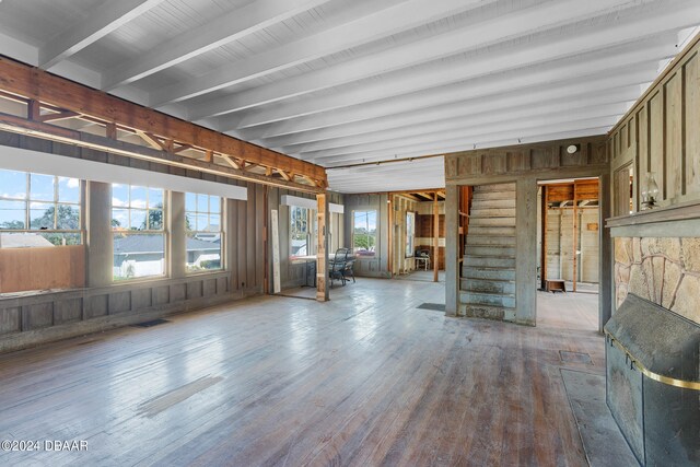 unfurnished living room featuring wood walls, wood-type flooring, beamed ceiling, and a fireplace