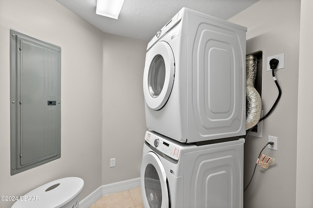 laundry room with a textured ceiling, electric panel, light tile patterned flooring, and stacked washer / drying machine