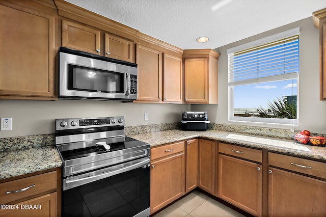 kitchen with a textured ceiling, appliances with stainless steel finishes, light tile patterned floors, and light stone counters