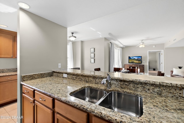 kitchen featuring ceiling fan, sink, light stone counters, and light tile patterned floors