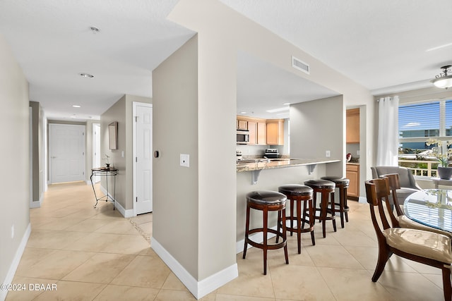 kitchen featuring light brown cabinetry, kitchen peninsula, light tile patterned floors, and a kitchen breakfast bar