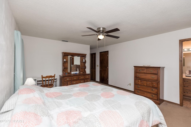 bedroom with ceiling fan, ensuite bathroom, light carpet, and a textured ceiling