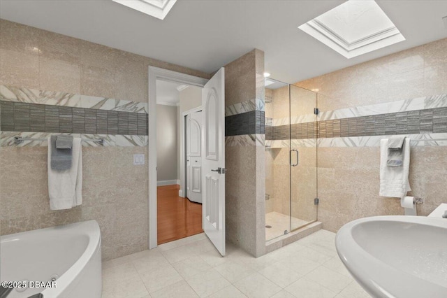 full bathroom with a skylight, a stall shower, tile walls, and a garden tub