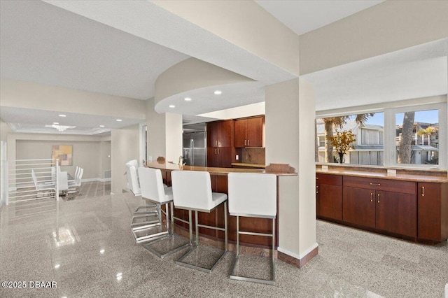 kitchen featuring a kitchen breakfast bar, granite finish floor, recessed lighting, decorative backsplash, and baseboards