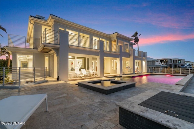 back of property at dusk with a patio area, stucco siding, a balcony, and a fenced in pool