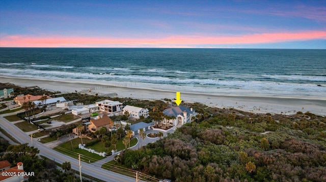 aerial view at dusk featuring a view of the beach and a water view