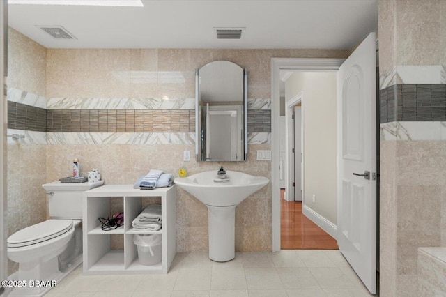 bathroom with tile patterned floors, visible vents, toilet, and tile walls