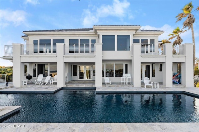 rear view of property featuring a patio area, an outdoor pool, and a balcony