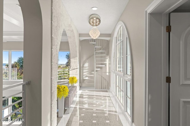 corridor featuring a notable chandelier, arched walkways, and plenty of natural light