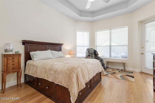 bedroom with ceiling fan, multiple windows, light hardwood / wood-style floors, and a raised ceiling