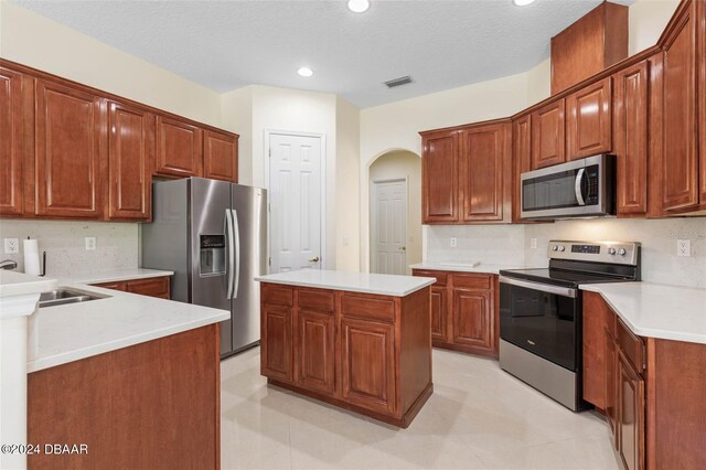 kitchen with stainless steel appliances, sink, tasteful backsplash, a textured ceiling, and a kitchen island