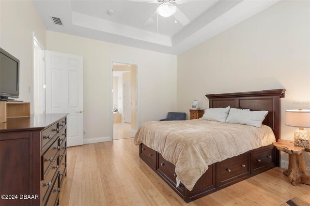 bedroom featuring light hardwood / wood-style floors, ceiling fan, and a raised ceiling