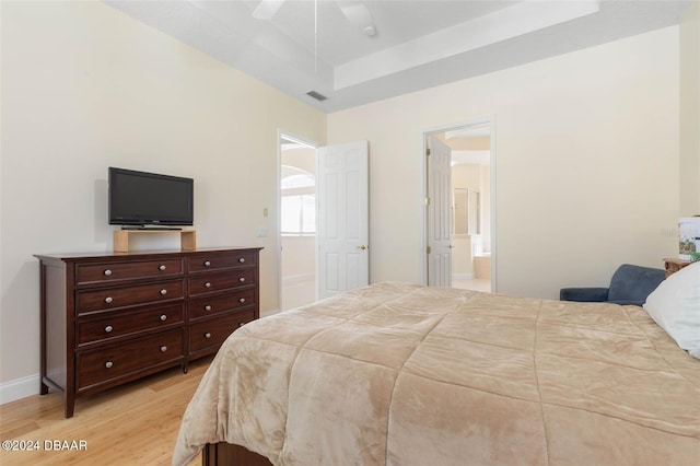 bedroom featuring ensuite bathroom, a tray ceiling, ceiling fan, and light hardwood / wood-style flooring