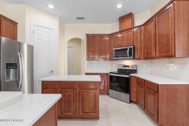 kitchen with decorative backsplash, stainless steel appliances, a textured ceiling, and a kitchen island