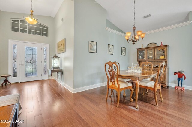 dining space with hardwood / wood-style floors, a notable chandelier, crown molding, and high vaulted ceiling