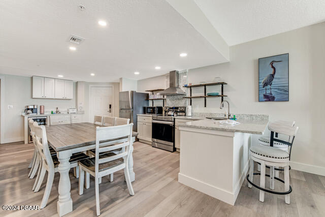 350 N Atlantic Ave Unit 2124, Daytona Beach, FL 32118 - kitchen with white cabinets, light hardwood / wood-style floors, wall chimney exhaust hood, and appliances with stainless steel finishes