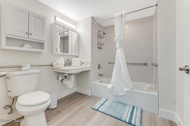 350 N Atlantic Ave Unit 2124, Daytona Beach, FL 32118 - bathroom featuring a textured ceiling, hardwood / wood-style flooring, toilet, and shower / bathtub combination with curtain