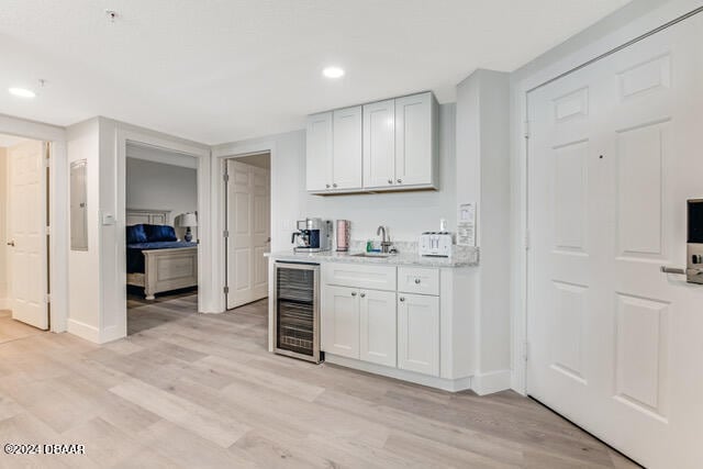 350 N Atlantic Ave Unit 2124, Daytona Beach, FL 32118 - bar with wine cooler, white cabinetry, sink, and light wood-type flooring