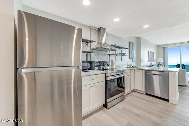 350 N Atlantic Ave Unit 2124, Daytona Beach, FL 32118 - kitchen featuring white cabinetry, appliances with stainless steel finishes, light hardwood / wood-style floors, and wall chimney range hood