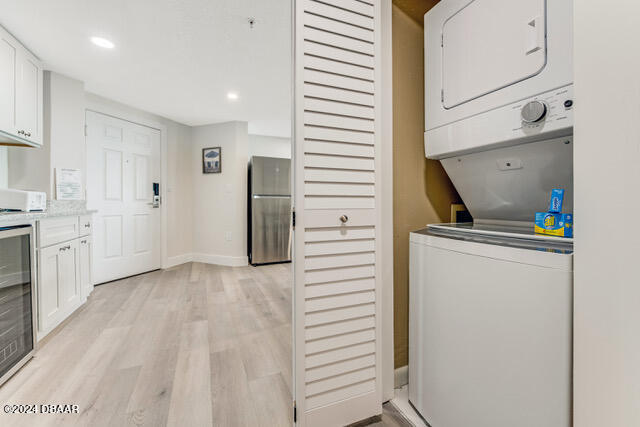 350 N Atlantic Ave Unit 2124, Daytona Beach, FL 32118 - laundry room with light hardwood / wood-style flooring, stacked washer and clothes dryer, and wine cooler