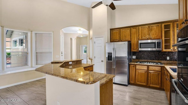 kitchen with a center island, backsplash, high vaulted ceiling, appliances with stainless steel finishes, and light stone counters