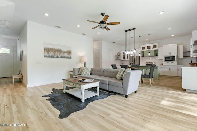 living room featuring light hardwood / wood-style flooring, ceiling fan, and sink