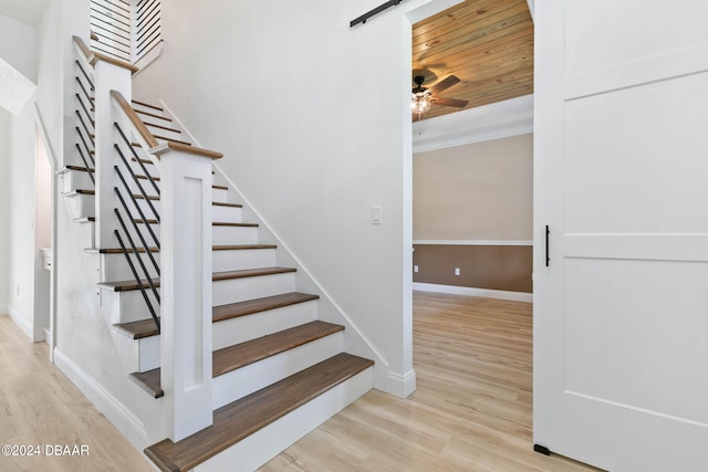 staircase featuring wood-type flooring, a barn door, crown molding, and ceiling fan