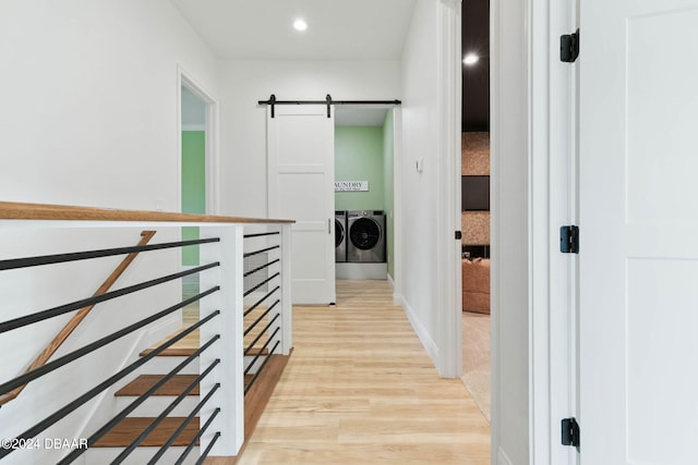 corridor with light wood-type flooring, a barn door, and separate washer and dryer