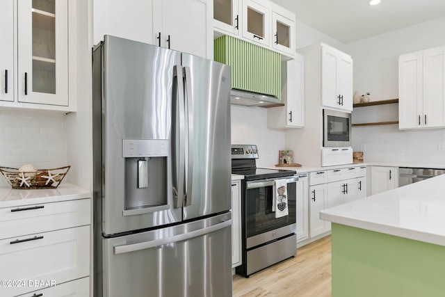 kitchen featuring appliances with stainless steel finishes, light stone countertops, decorative backsplash, white cabinets, and light hardwood / wood-style flooring